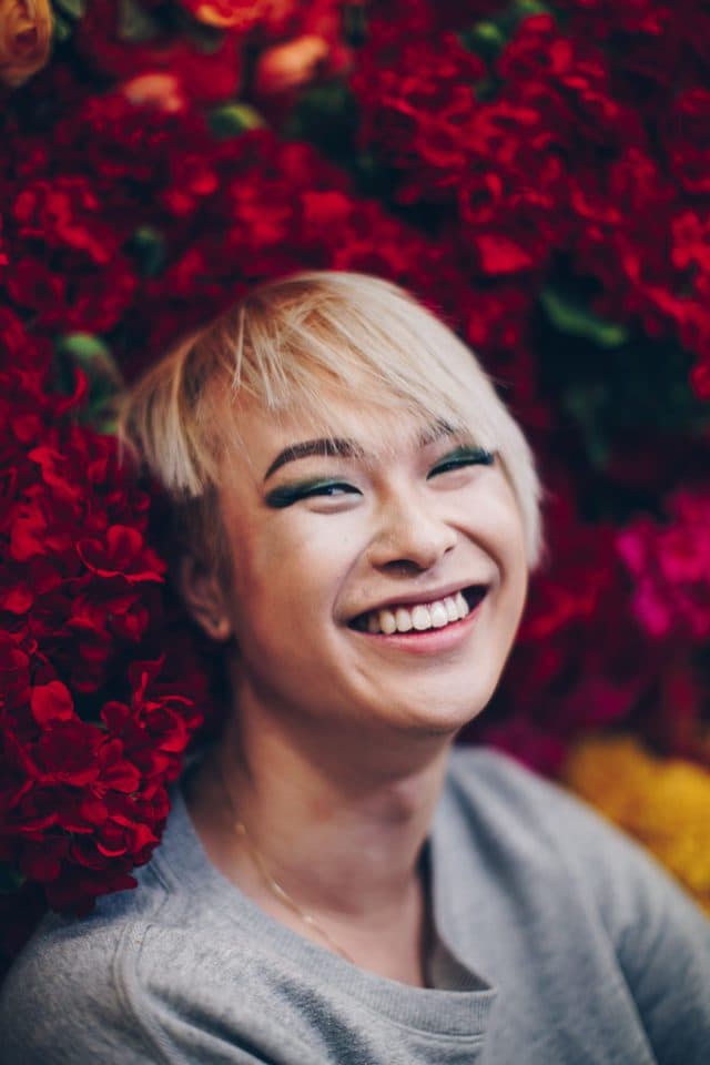 Portrait by Charmaine: a laughing subject against a wall of red flowers