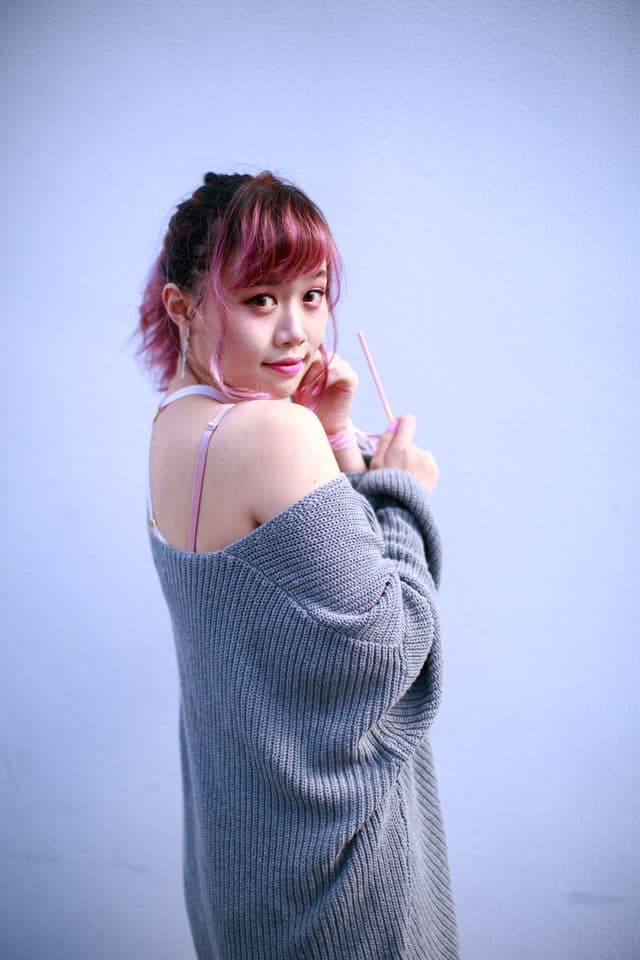 Portrait by Charmaine: a subject with pink hair against a lavender wall